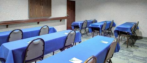 A conference room with multiple tables covered in blue tablecloths, arranged in rows with chairs.