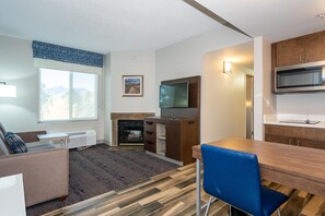 Una sala de estar moderna con chimenea, televisor de pantalla plana y comedor con mesa de madera y sillas azules.