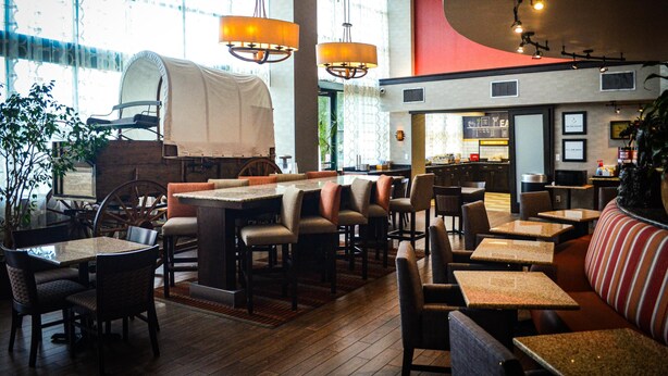 En restaurang med högt i tak, stora fönster och ett varierat utbud av sittplatser, inklusive bord, avskilda bås och en bardisk.