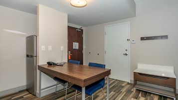 Una habitación pequeña y moderna con una mesa de madera, sillas azules, un armario blanco y un refrigerador.