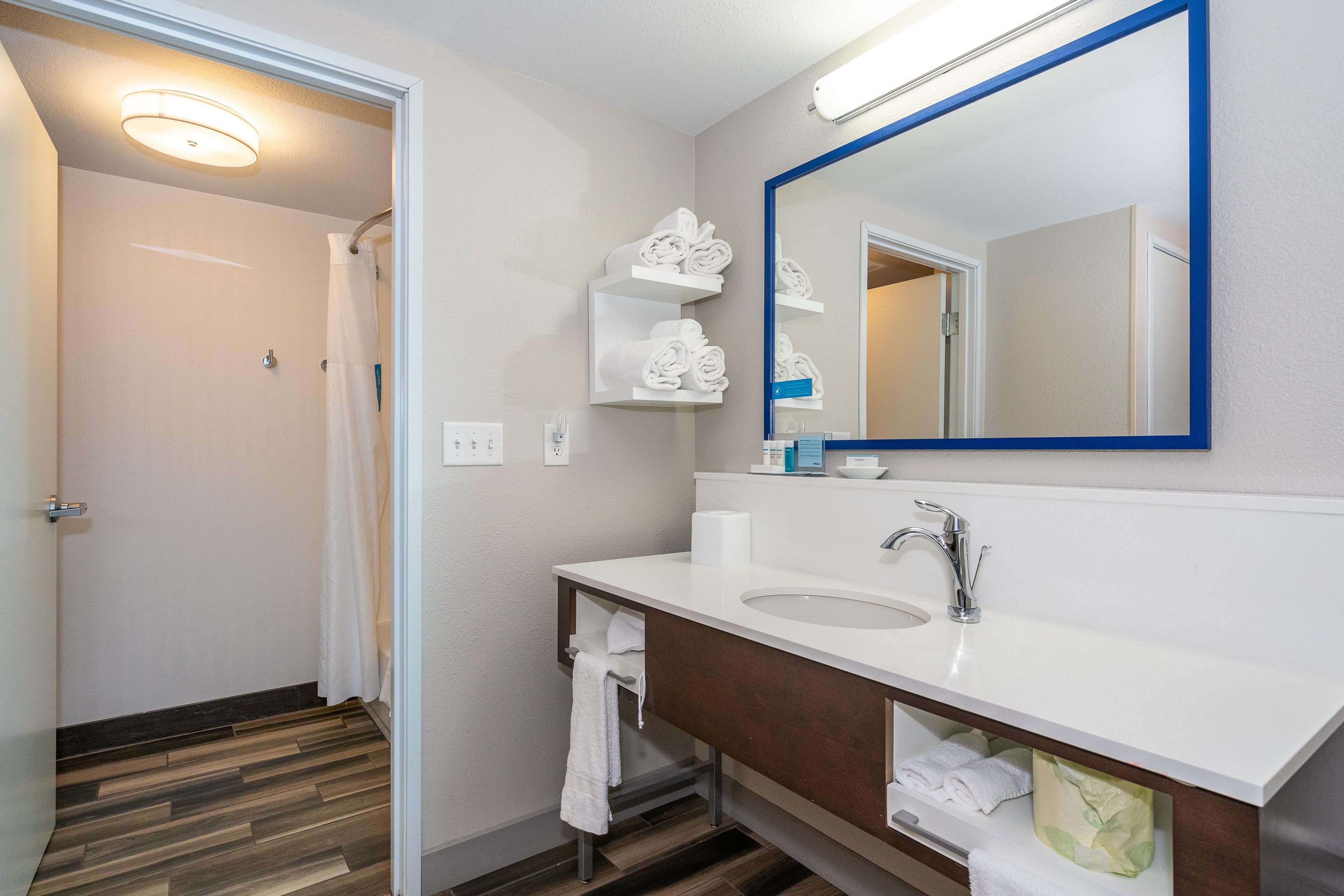 A bathroom with a white sink, a mirror with a blue frame, and shelves with rolled towels.