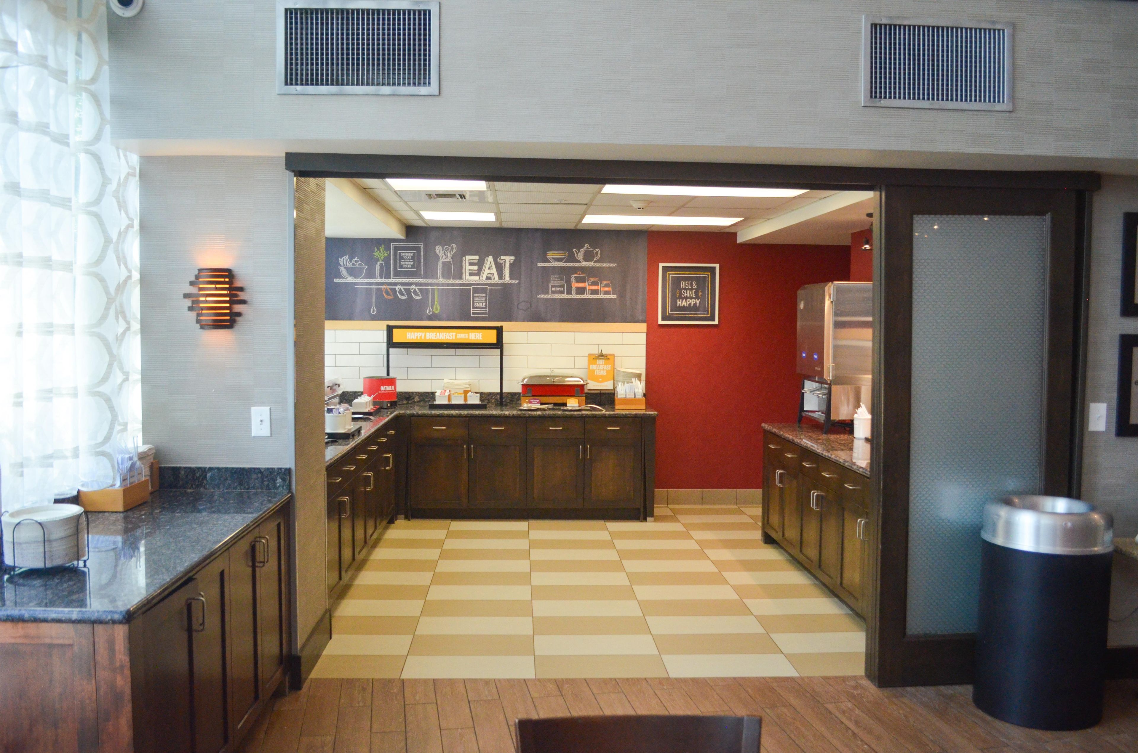A breakfast area with a checkered floor, a counter with a sign that says 'HAPPY BREAKFAST HERE', and a wall with a chalkboard menu.