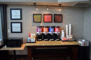 A coffee station with four coffee dispensers labeled Decaf Roast, Light Roast, Dark Roast, and Hot Water. There are framed signs on the wall and a microwave on the counter.