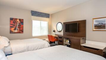 Ein Hotelzimmer mit zwei Betten, einem Schreibtisch, einem Sessel, einem Fernseher und Bildern an der Wand.