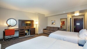 Ett hotellrum med två sängar, ett skrivbord med en stol, en soffa, en TV och en spegel.