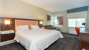 Habitación de hotel con una cama grande, dos mesitas de noche con lámparas, un escritorio con silla, una ventana y aire acondicionado de pared.