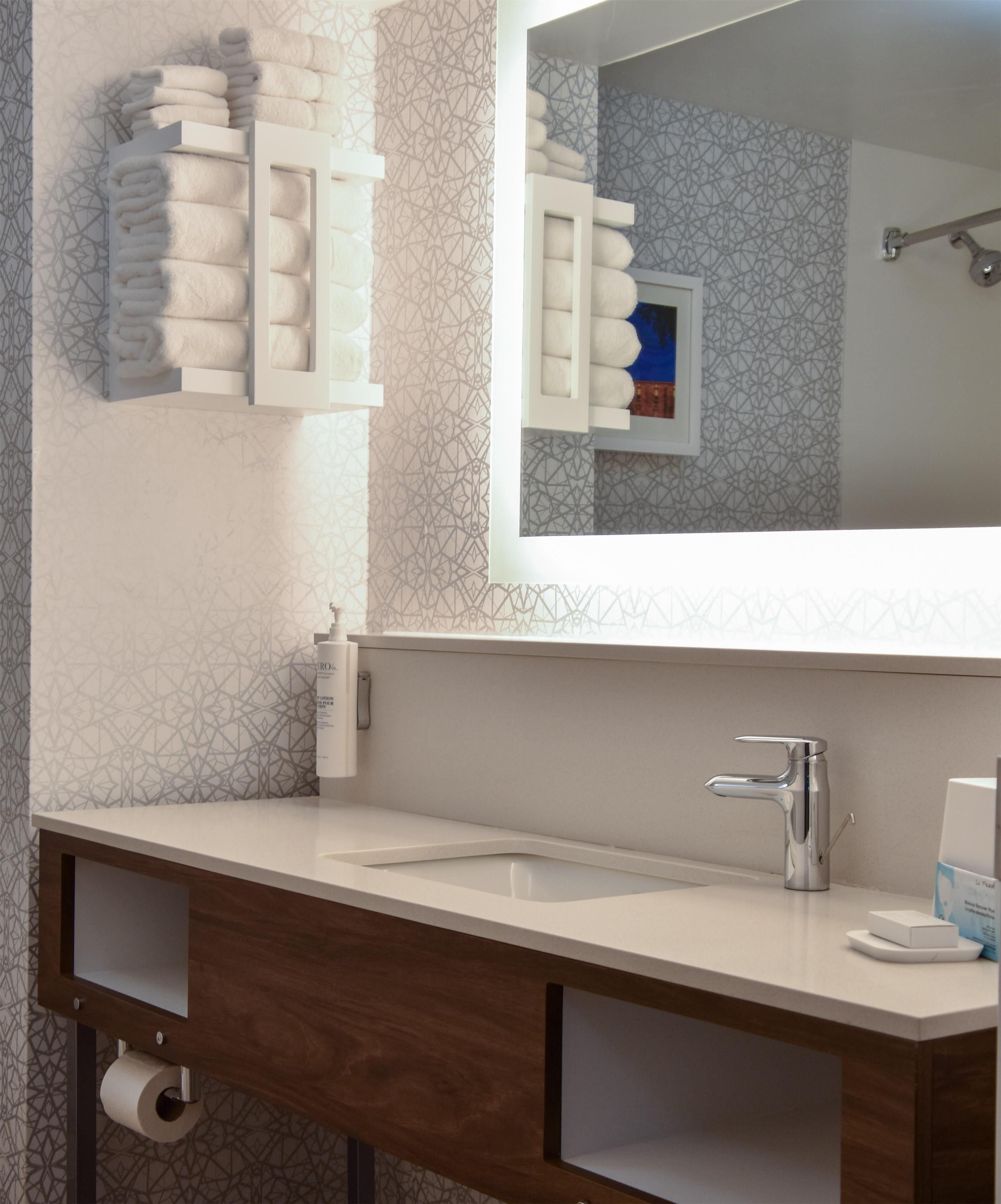 Un baño con un lavamanos blanco, un espejo y un perchero con toallas dobladas.