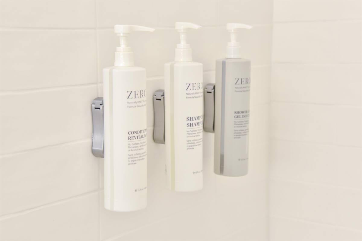 Tre bottiglie di shampoo e balsamo Zero su un muro piastrellato di bianco.
