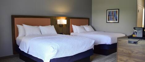 Una habitación de hotel con dos camas, una mesita de noche, una lámpara y un cuadro en la pared.
