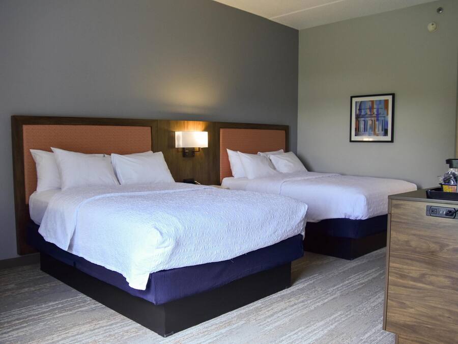 A hotel room with two beds, a nightstand, a lamp, and a painting on the wall.