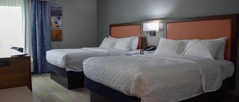 Een hotelkamer met twee bedden, een bureau en een raam met gordijnen.