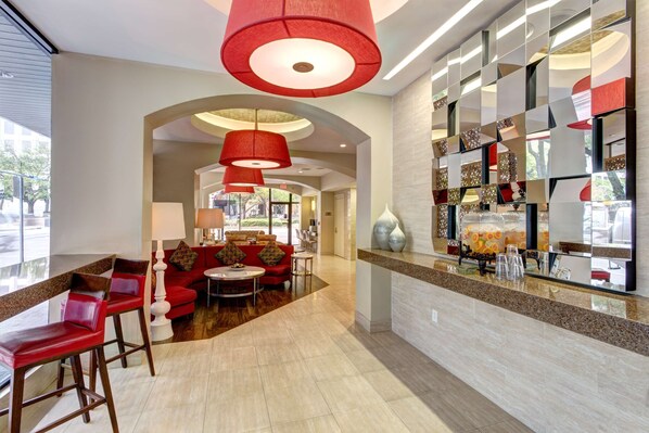 A modern lobby with red bar stools, a red sofa, and a coffee bar with a mirror and decorative items.