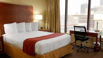 Een hotelkamer met een groot bed, een bureau, een stoel en uitzicht op de stad door het raam.