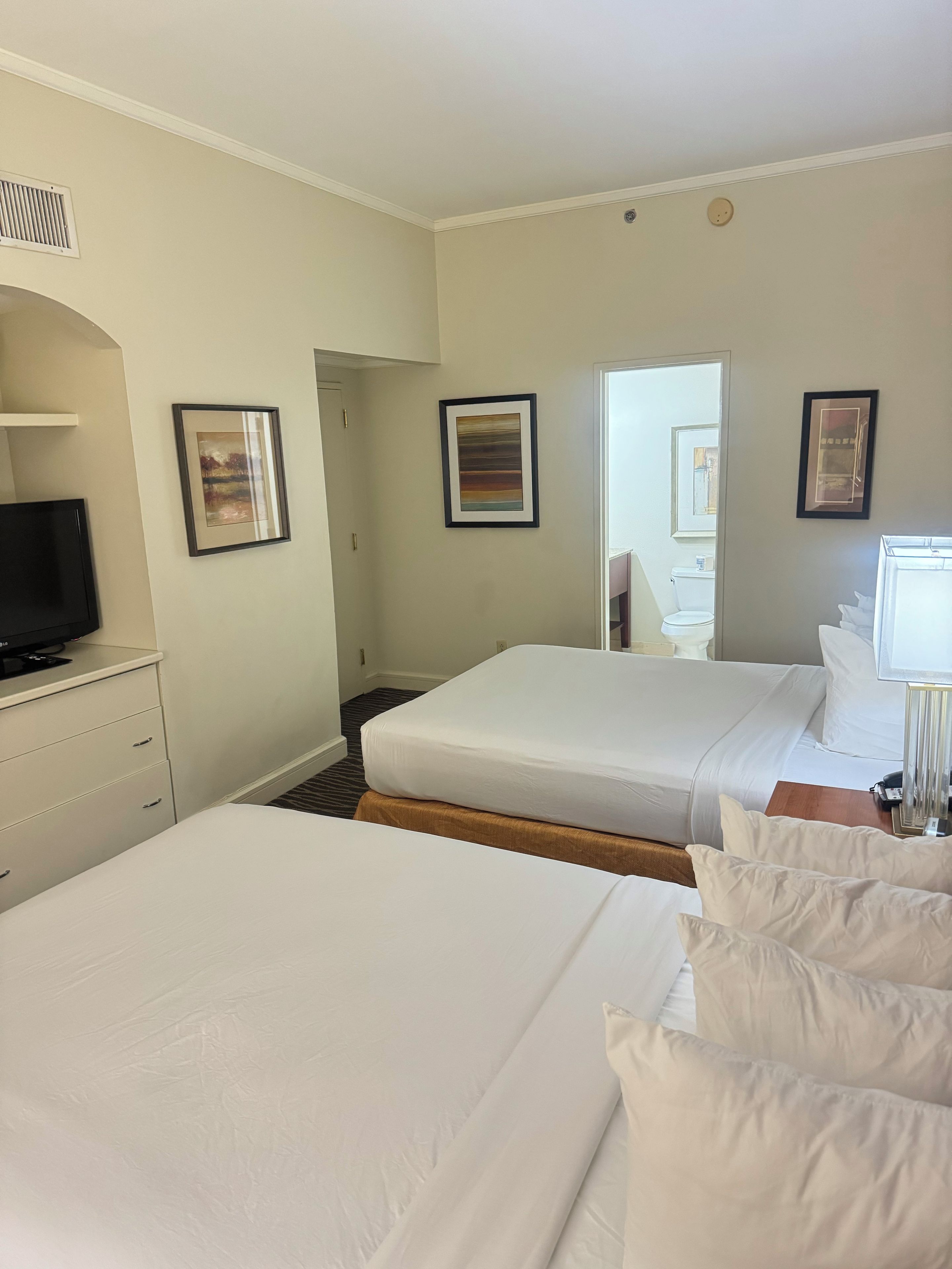 A hotel room with two beds, a television, and framed artwork on the walls.