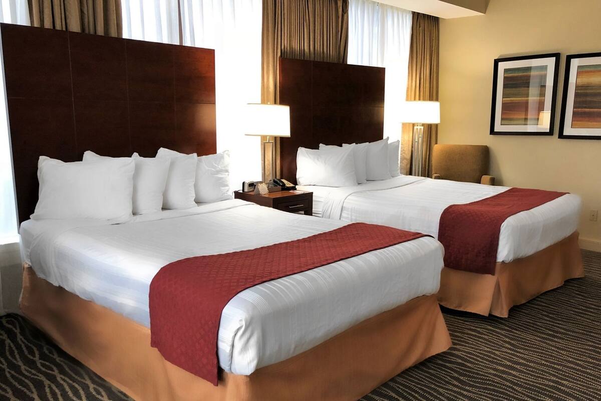 A hotel room with two beds, a nightstand, a lamp, and a chair.