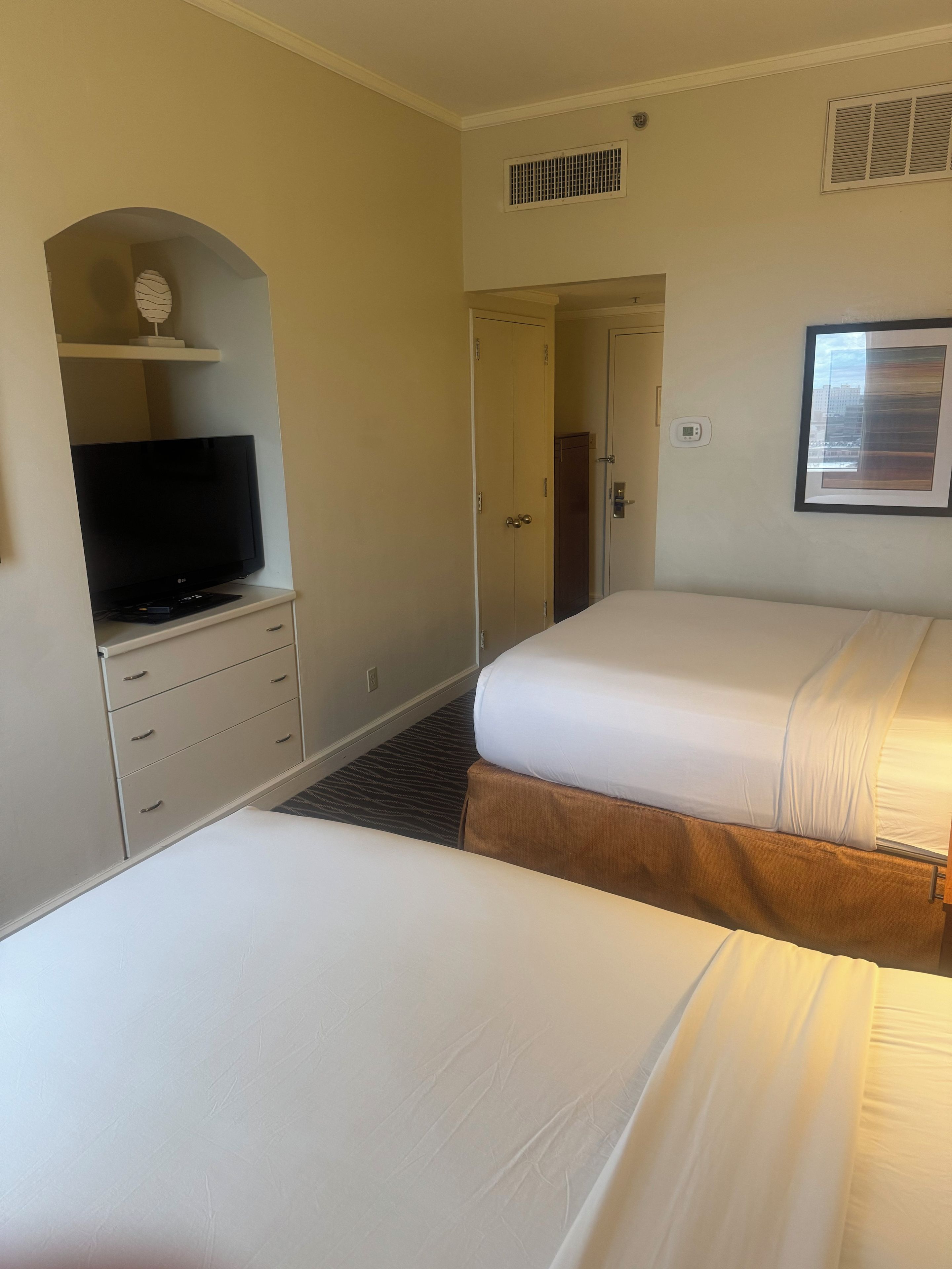 A hotel room with two beds, a television on a dresser, a door, and a window with blinds.