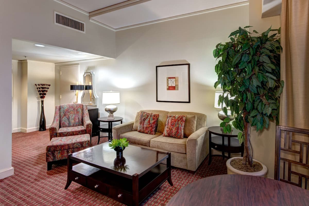 A living room with a sofa, armchairs, a coffee table, a potted plant, and a framed picture on the wall.