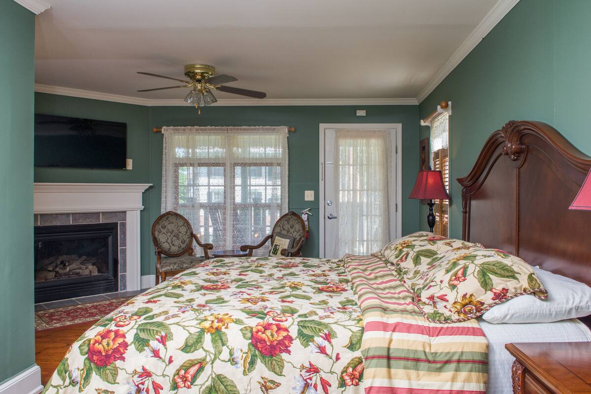 A bedroom with a large floral bedspread, a wooden headboard, a fireplace, and a ceiling fan.