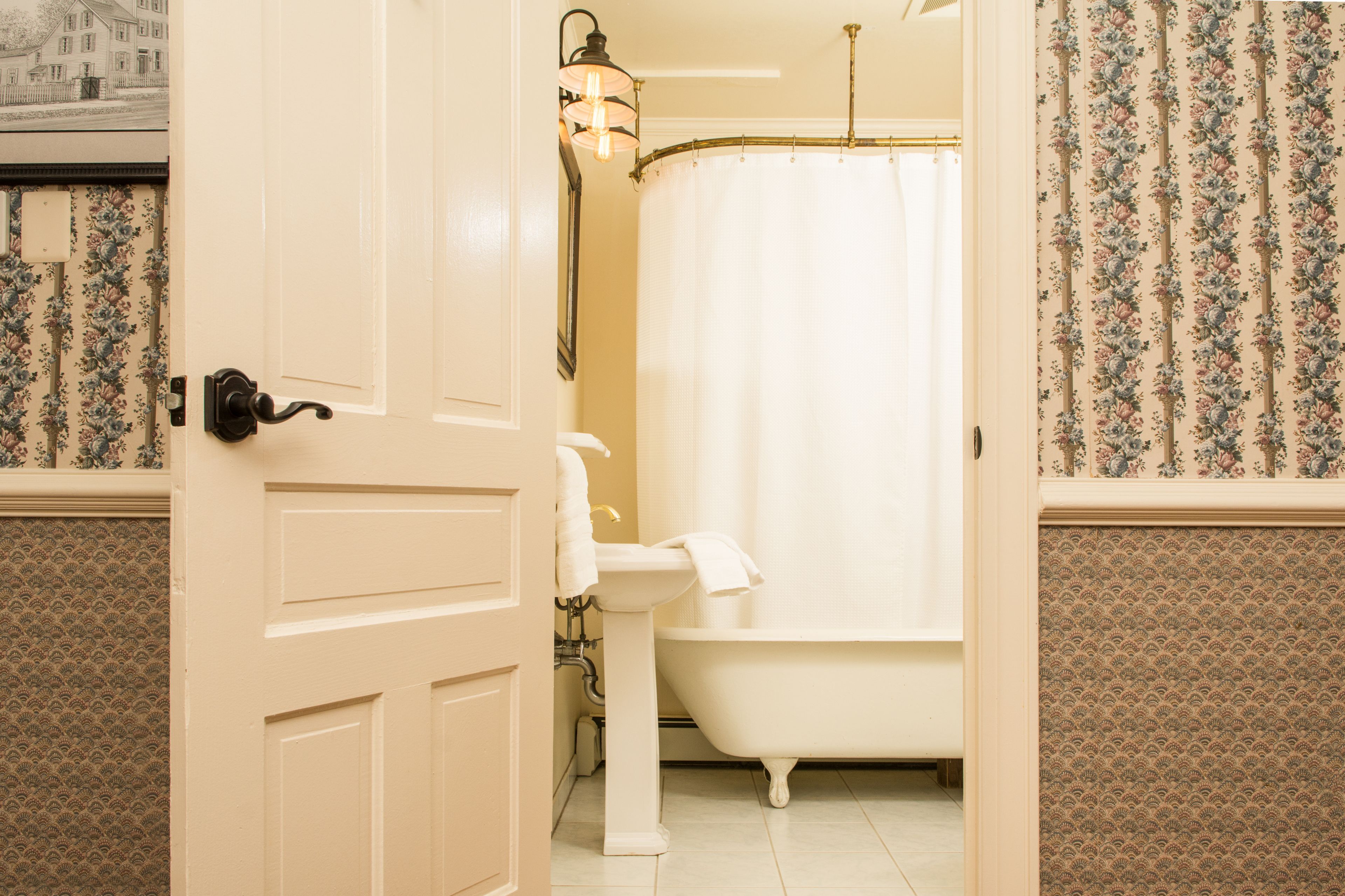 A bathroom with a white door, a sink, a bathtub, and a shower curtain.