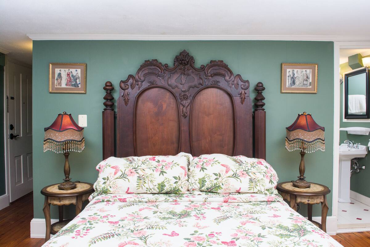 A bedroom with a large bed, two bedside tables with lamps, a wooden headboard, and a wall-mounted mirror.