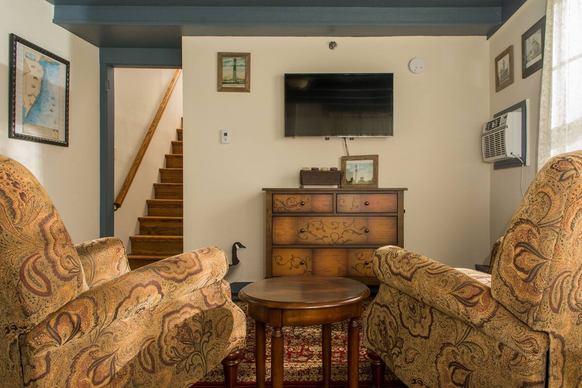 A living room with patterned sofas, a wooden coffee table, a flat-screen TV, and a staircase leading upstairs.