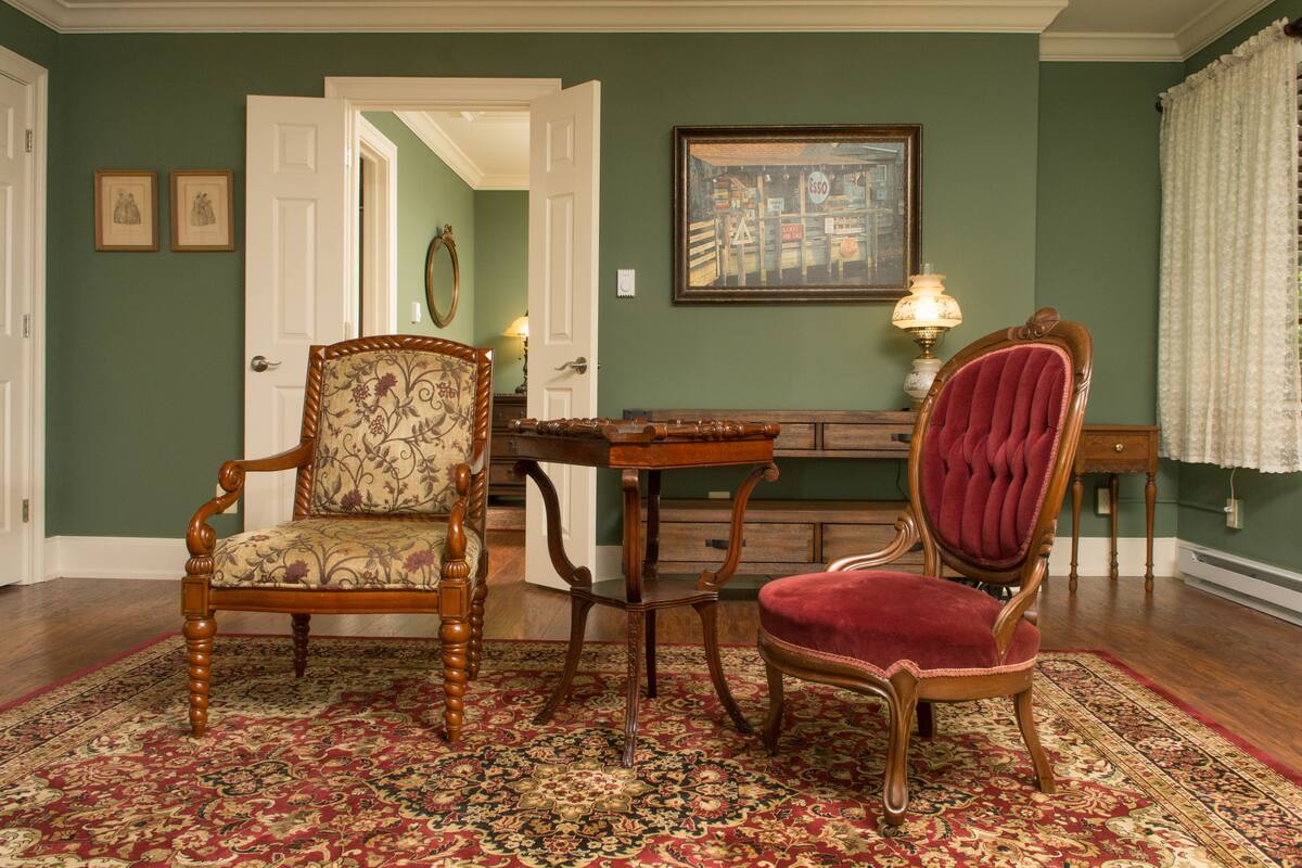 A room with a wooden chair, a red velvet chair, a table, and a patterned rug.
