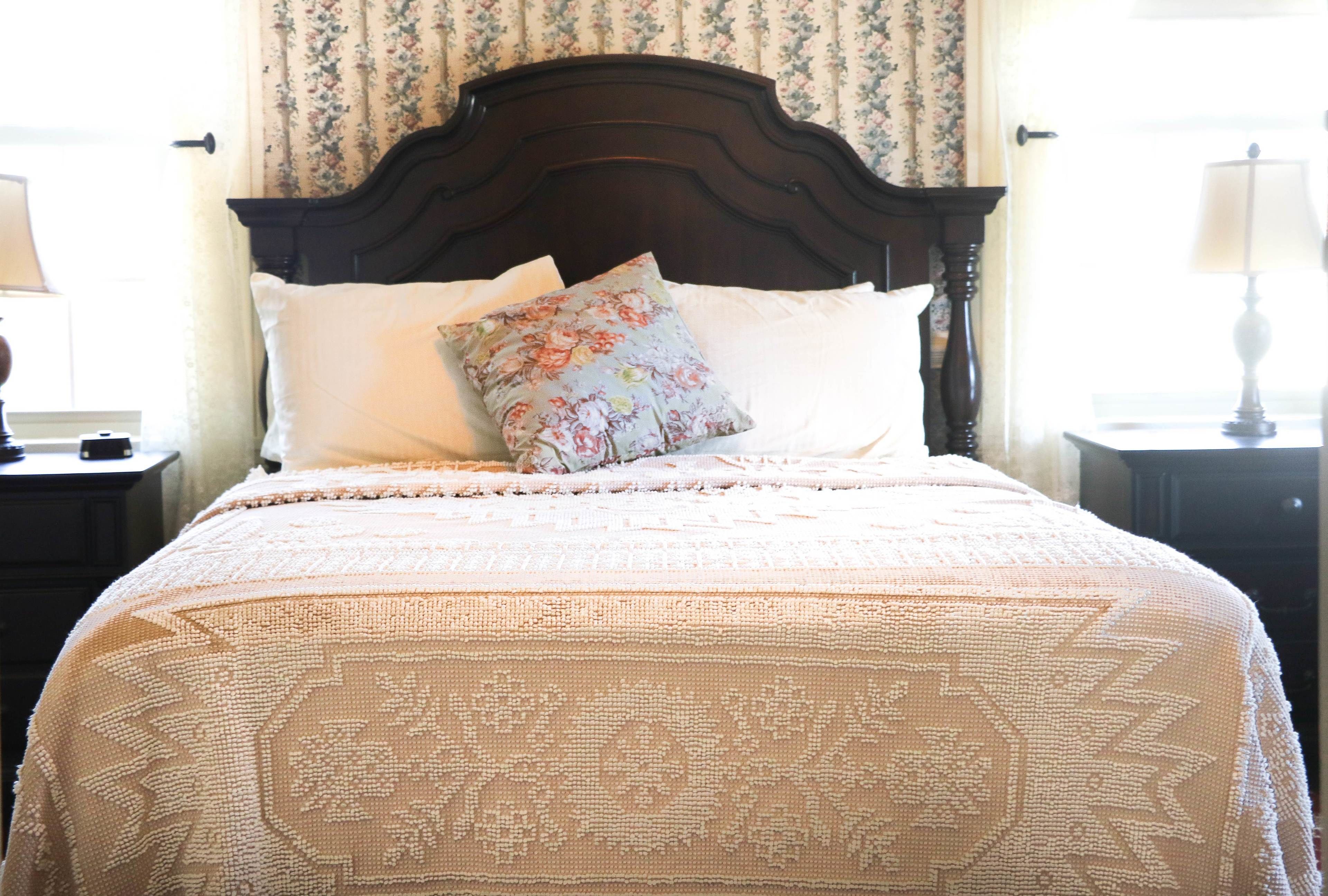 Cama bem arrumada com travesseiro floral e colcha estampada em quarto com papel de parede floral e cabeceira de madeira escura.