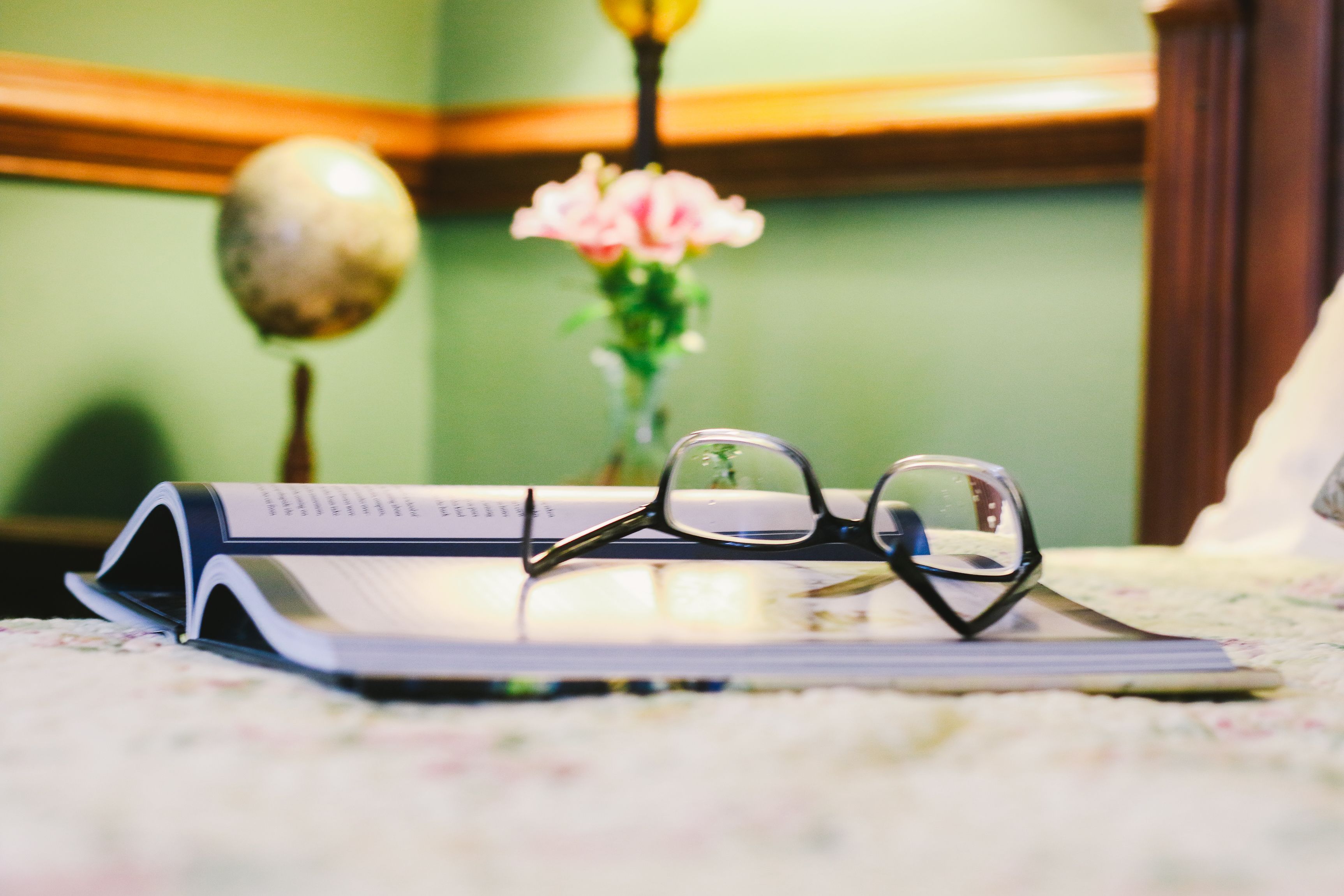 A book, glasses, and a vase with flowers on a table.