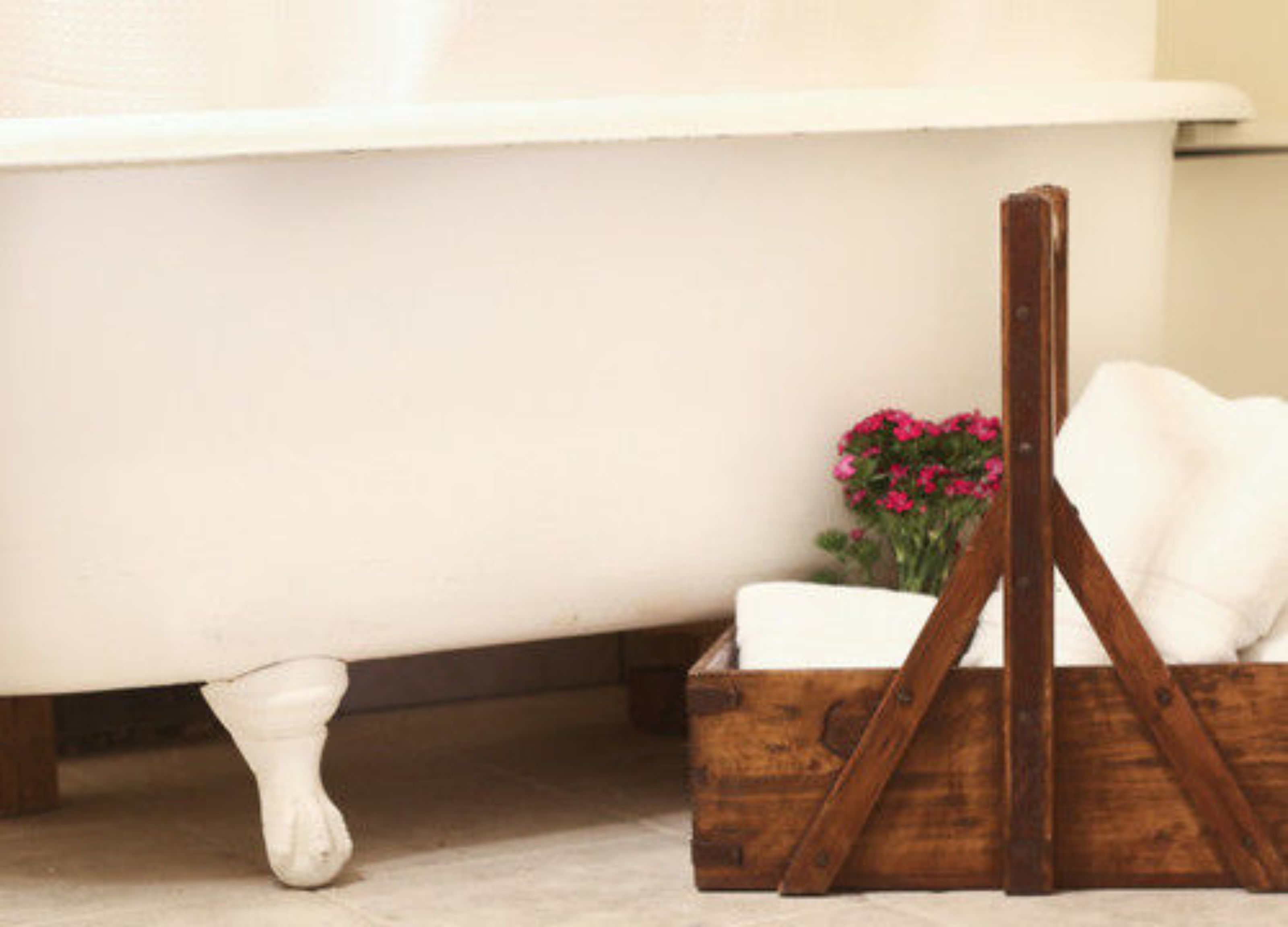 A white bathtub with a wooden crate and pink flowers beside it.