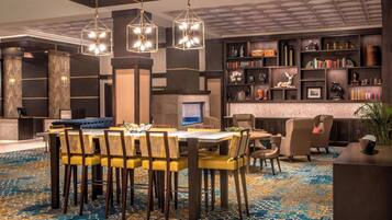 Un hall d’hôtel moderne comprenant un espace repas, une cheminée et une bibliothèque remplie de livres et d’objets décoratifs.