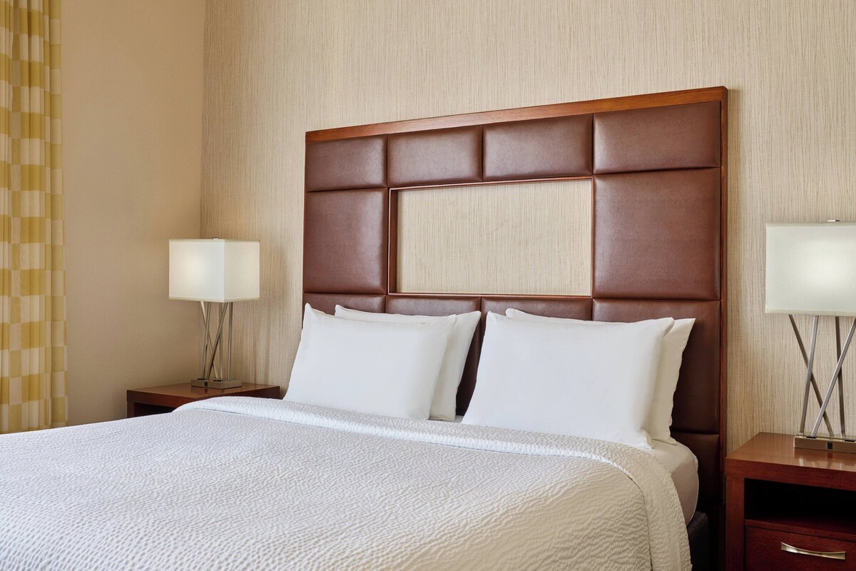 A hotel room with a large bed, two bedside tables, and a headboard with a padded design.