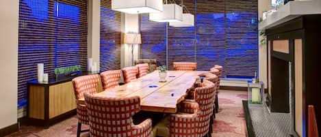 A conference room with a long table, red and white checkered chairs, and large windows with blue blinds.