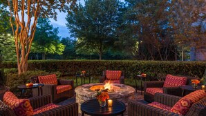 An outdoor seating area with wicker furniture, a stone fire pit, and a hedge in the background. - Hilton Garden Inn Atlanta North/Alpharetta (Alpharetta)