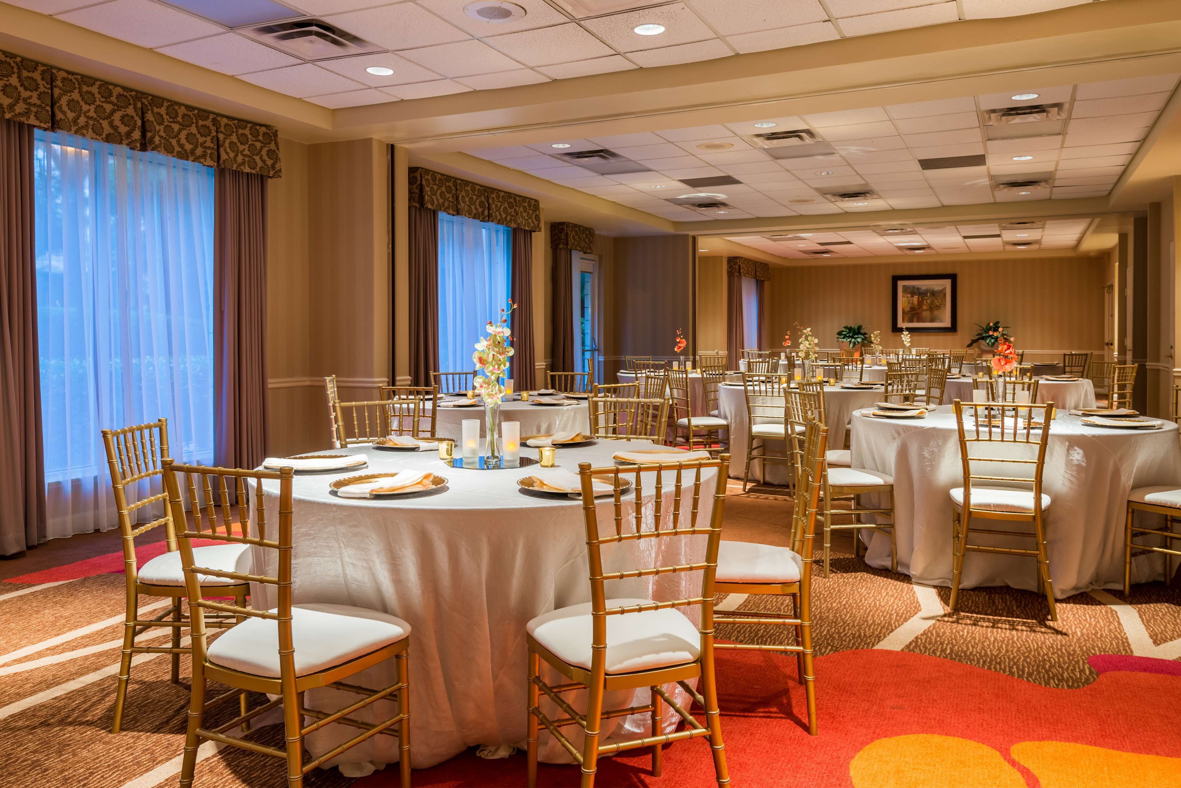 Un salón de banquetes con mesas redondas, sillas doradas y manteles blancos.