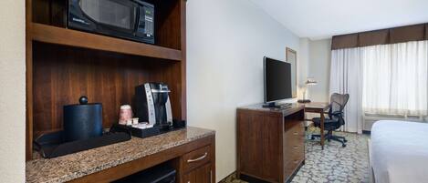 A hotel room with a kitchenette, a television, a desk with a chair, and a bed.