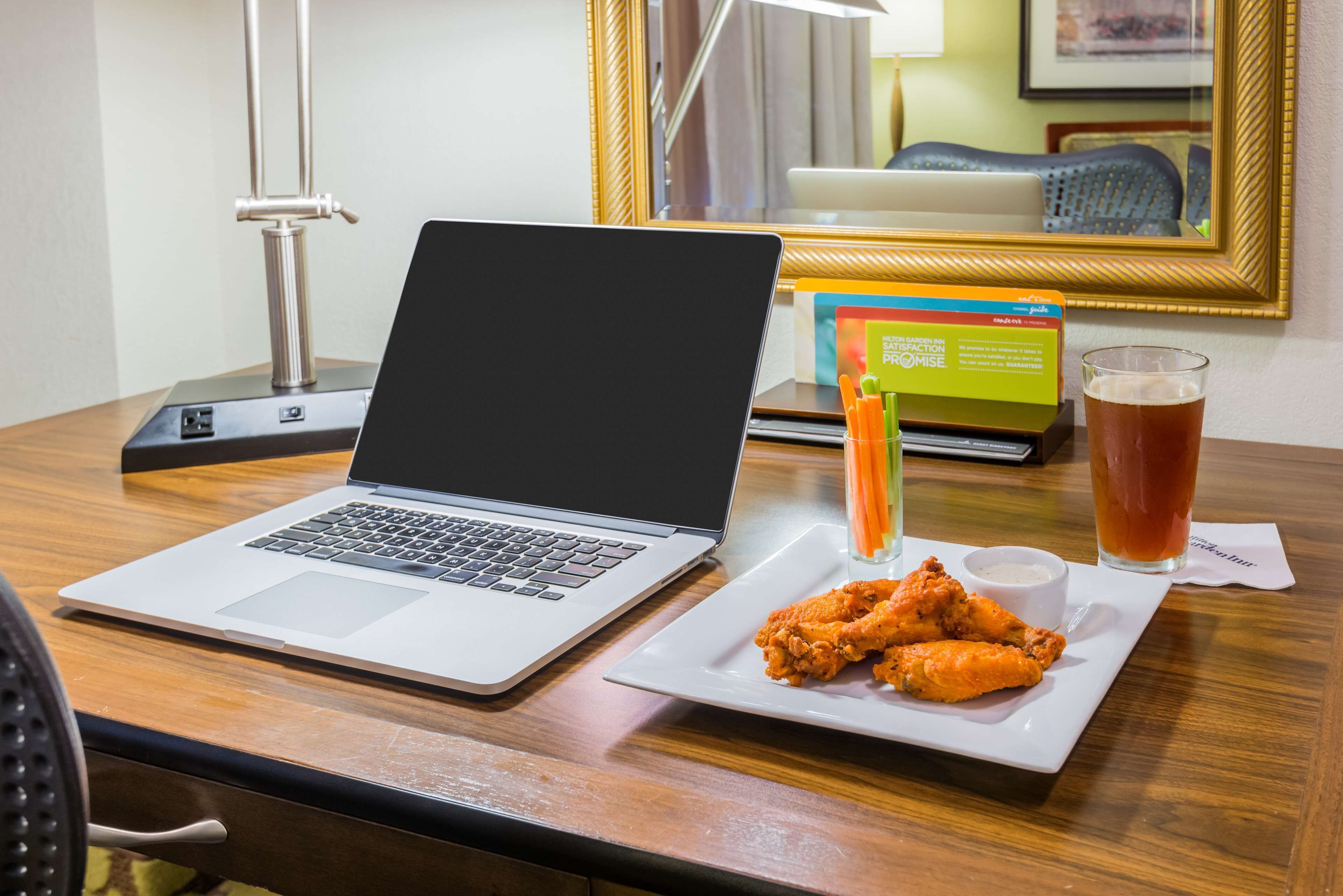 A laptop on a wooden table with a plate of chicken wings and a drink.