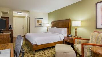 A hotel room with a bed, a desk with a computer, a chair, a small table, and a lamp.