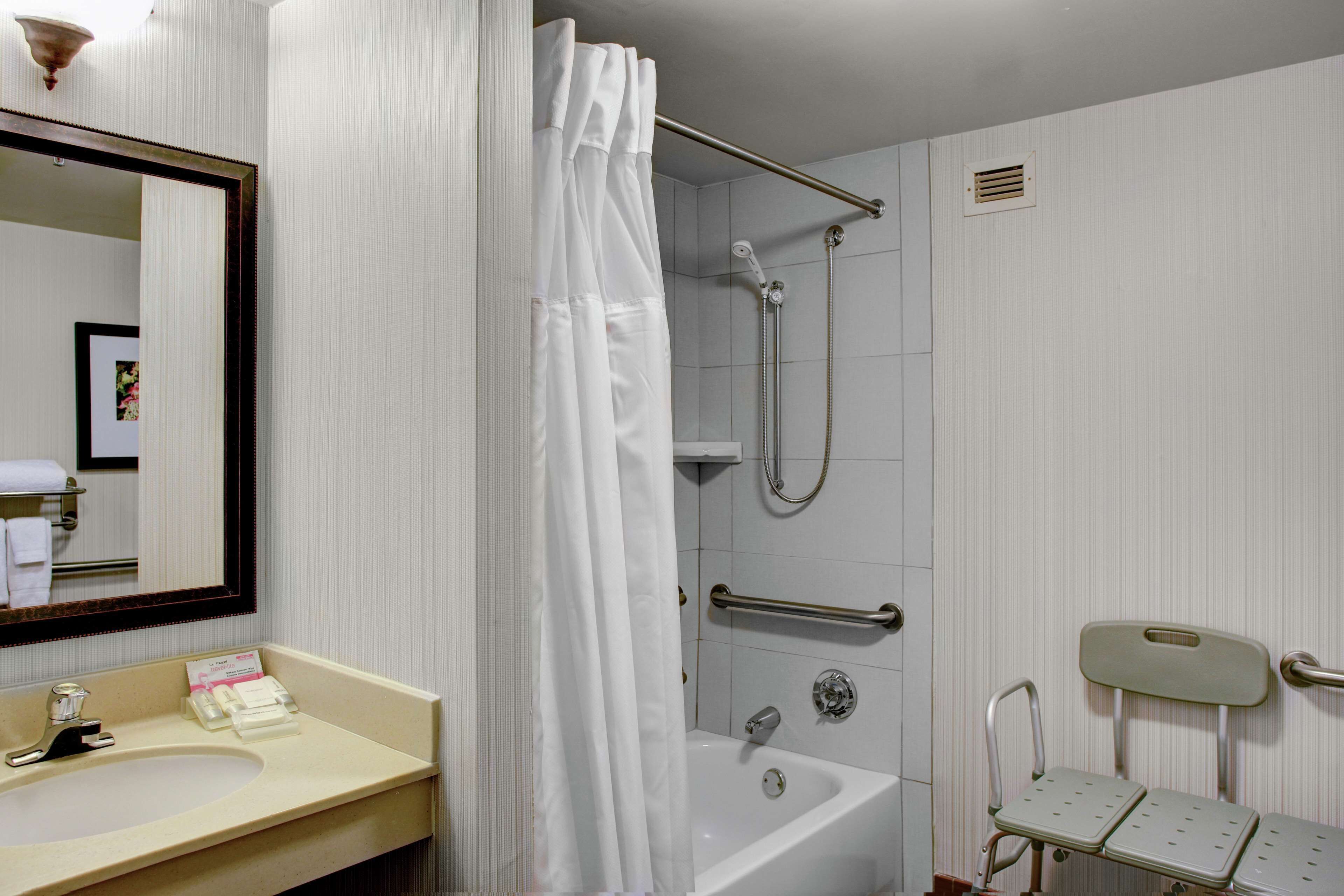 A bathroom with a sink, mirror, shower, and grab bars.
