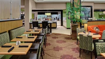 A hotel lobby with seating areas, a reception desk, and a kitchen in the background.