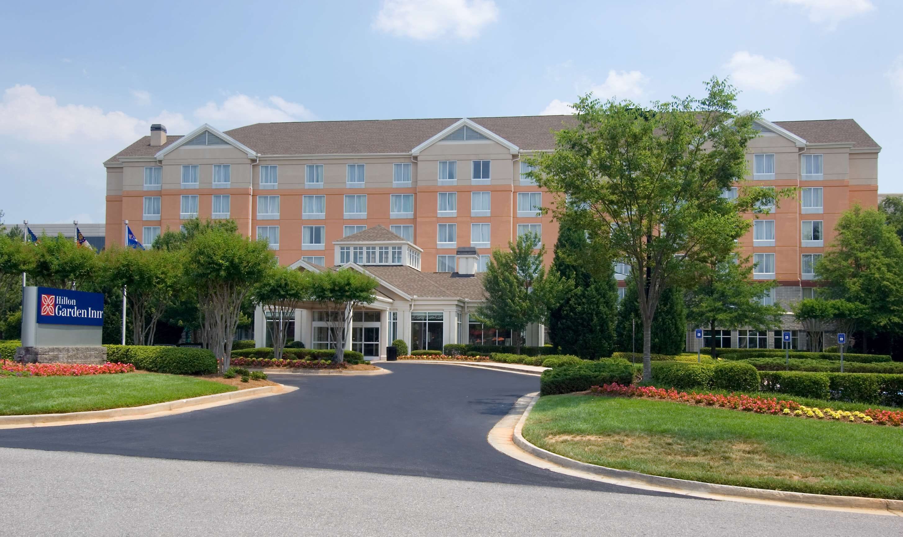 A large, multi-story hotel with a prominent entrance, surrounded by well-maintained landscaping and a clear sky.