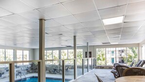 Un espace piscine intérieur doté de murs en verre transparent, d’un sol en pierre et d’une table de billard avec des chaises.