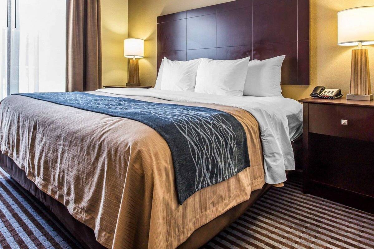 A hotel room with a large bed, a nightstand with a lamp, and a telephone.