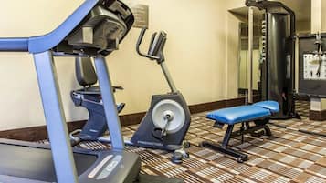 A hotel gym with cardio machines, a weight bench, and a mirror.