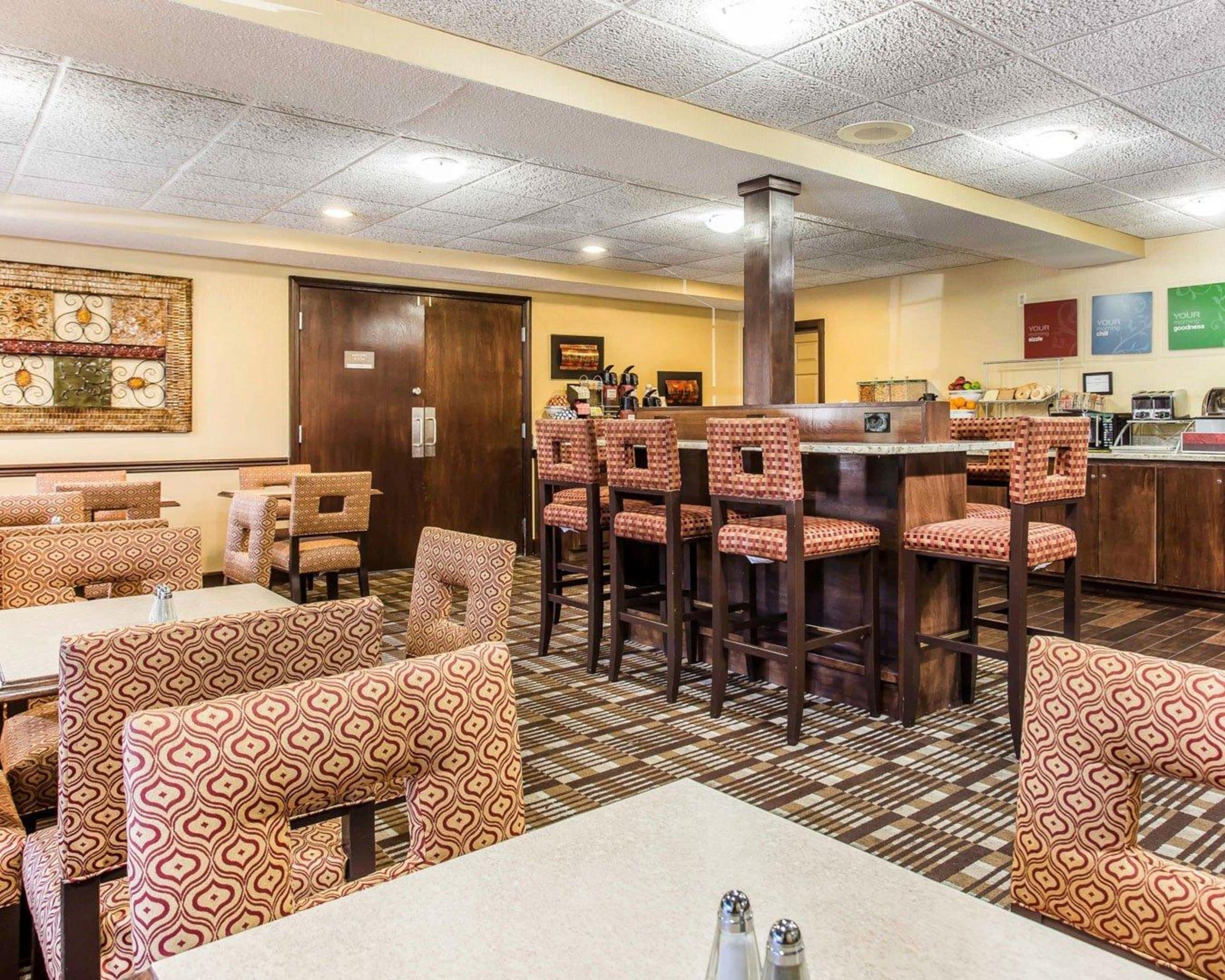 A restaurant with patterned booths and high stools, a bar area, and a tiled floor.