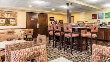 A restaurant with patterned booths and high stools, a bar area, and a tiled floor.