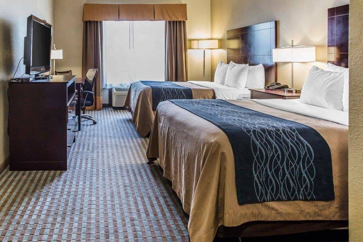 A hotel room with two beds, a desk with a TV, a chair, and a window with curtains.