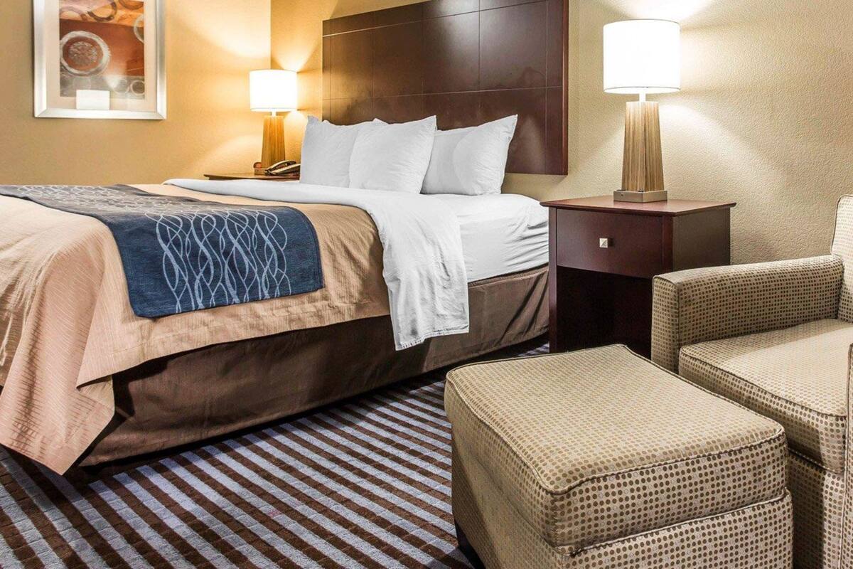 A hotel room with a large bed, two bedside tables, a headboard, a framed picture on the wall, and a patterned rug.