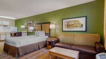 Une chambre d’hôtel avec un lit, un canapé, un bureau avec une lampe, une chaise et un tableau au mur.