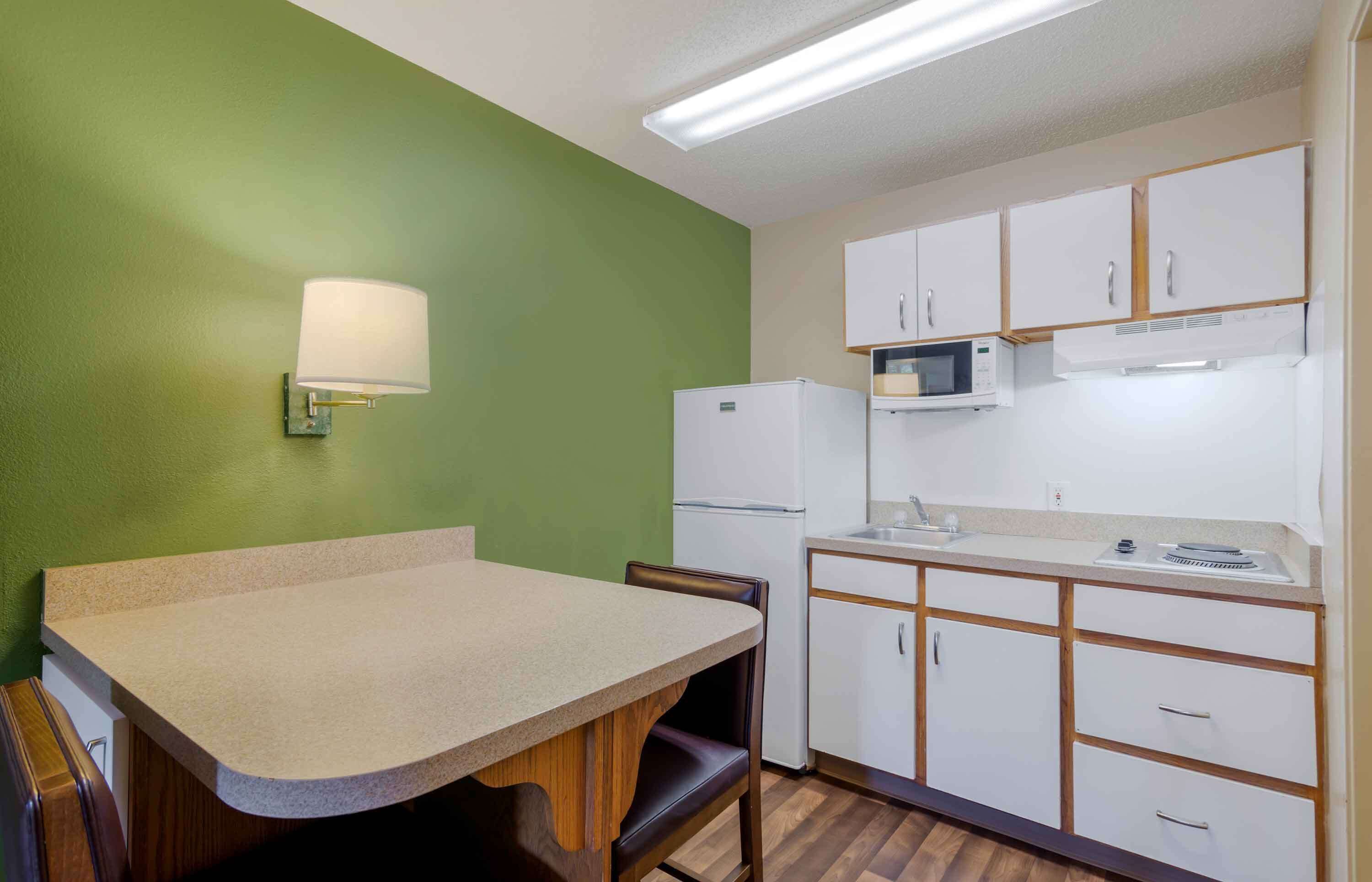 A compact kitchen with a green wall, white cabinets, a microwave, a refrigerator, and a small sink.