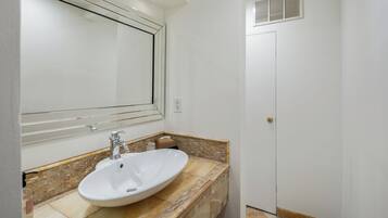 Een badkamer met een wit wastafelmeubel, een spiegel en een deur.